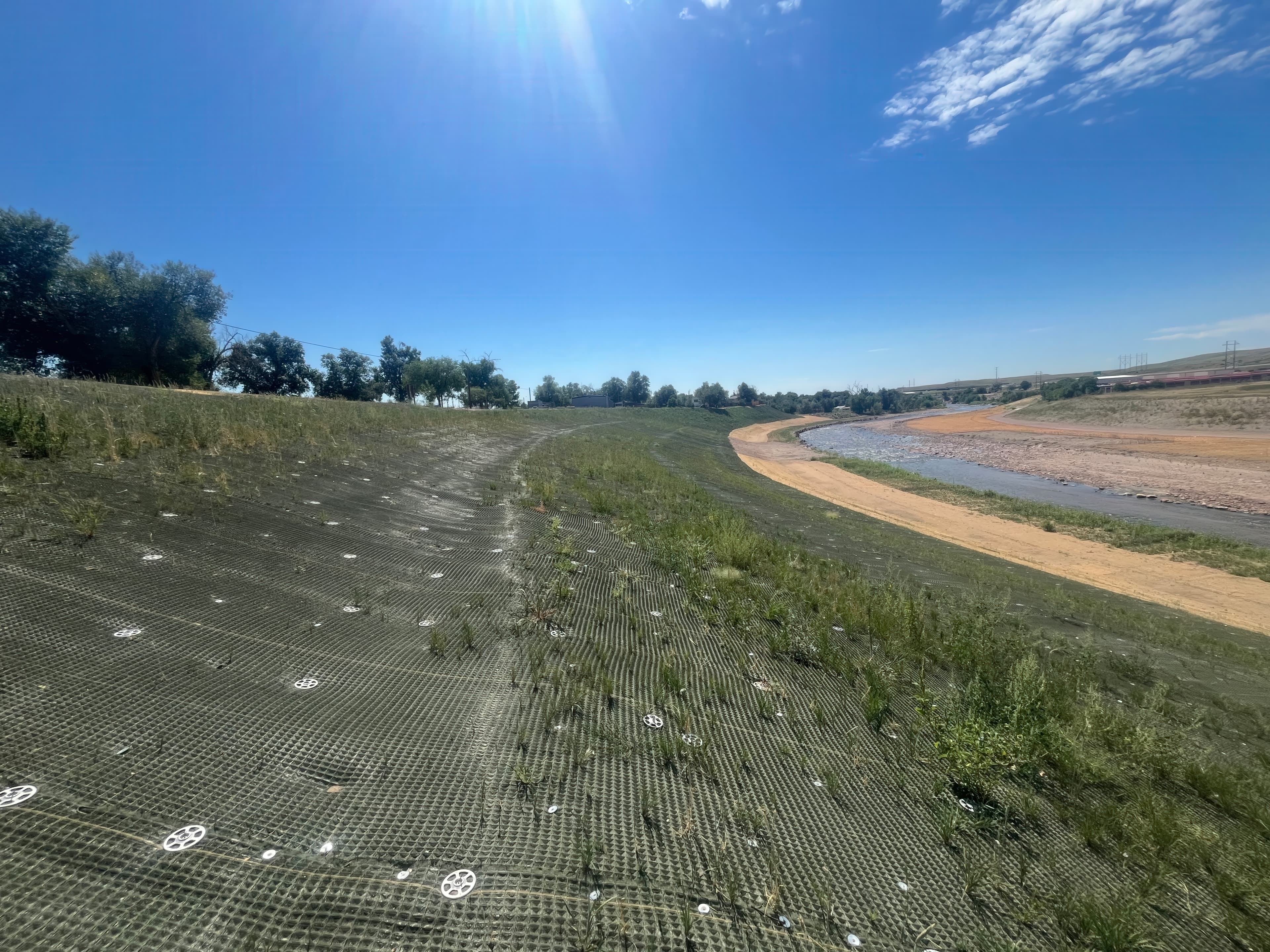 Slope preparation and seeding before PROPEX® Armormax® placement, ensuring vegetation roots interlock with the reinforcement mat for long-term slope stability.