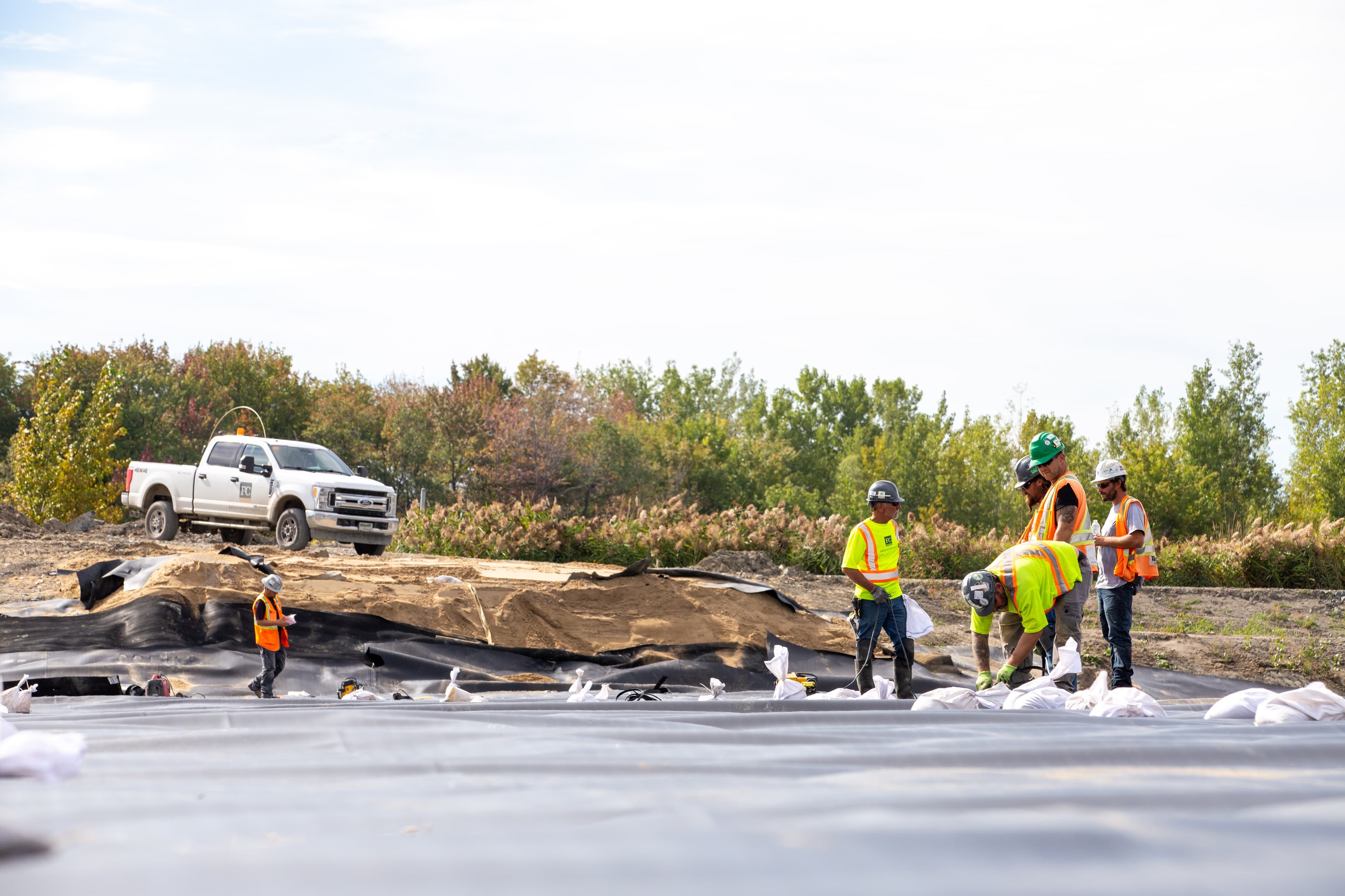 Field crew deploying 60-mil textured GSE HD liner manufactured in Varennes, ensuring high chemical resistance and low permeability for controlled contaminant migration.