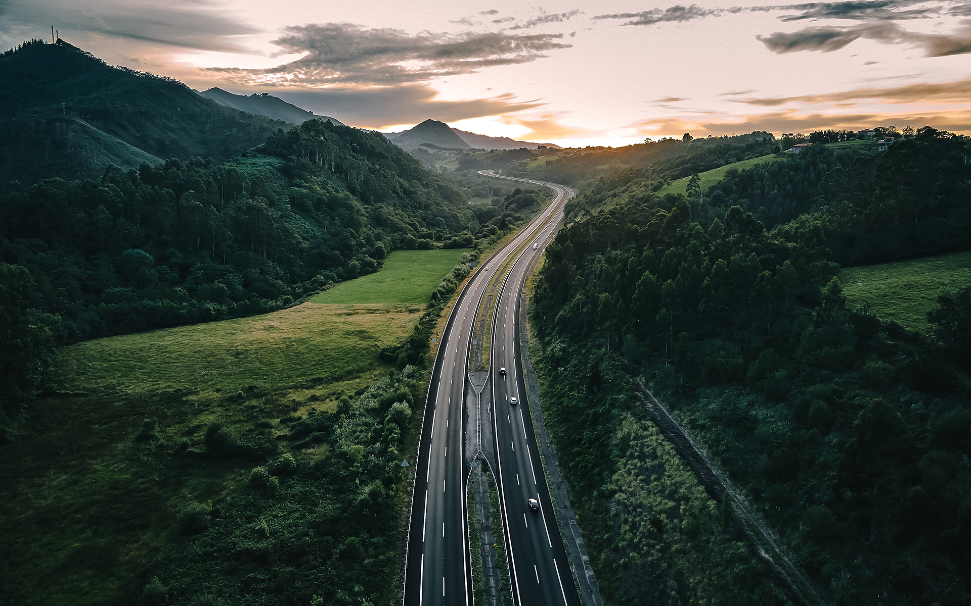 Aerial view of a highway cutting through lush green hills at sunset.